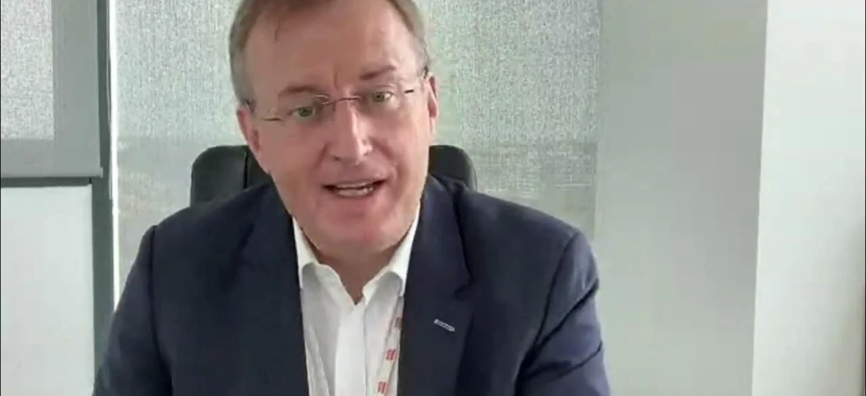 Adam Sikorski, pracownik umysłowy, nosi okulary i koszulę. Jego czoło i podbródek są widoczne powyżej kołnierza, gdy mówi jako rzecznik.